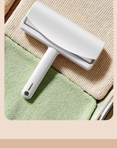 Close-up detail of a white manual lint roller placed on clean folded fabrics.