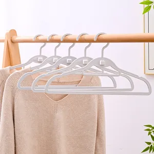 Weiße nahtlose Kunststoff-Kleiderbügel an einer Holzstange mit einem beigen Pullover