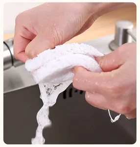 Close-up view of hands wringing water out of a white wood pulp cleaning sponge in a kitchen sink