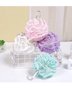 Detailed view of soft mesh bath loofahs in pastel colors with decorative pom-pom trim