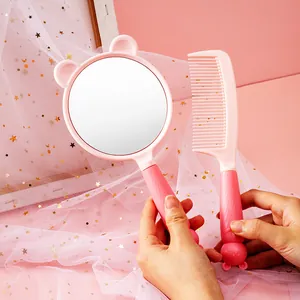 Close-up view of a pink cartoon handheld makeup mirror and matching comb set held by hands.