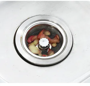 Close-up of stainless steel sink strainer plug with food residue in a kitchen sink.