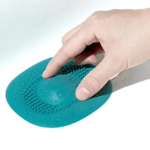 Close-up of teal silicone drain hair filter being pressed by a hand in a white sink.