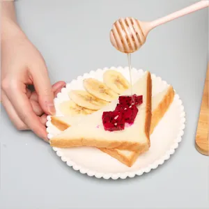 Pink plastic honey dipper stick dripping golden honey onto fresh toast and fruit breakfast