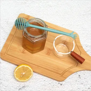 Teal plastic honey dipper wand on a wooden board with a honey jar and half lemon