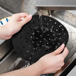 Reusable black perforated silicone air fryer liner being cleaned in a kitchen sink
