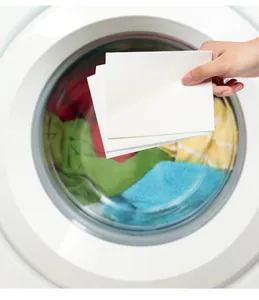 Hand holding three white anti-color-bleeding laundry sheets against a washing machine