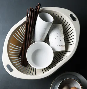 Cream oval plastic colander basket filled with chopsticks, bowls and ceramic cups