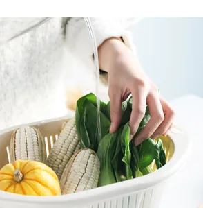 Close-up of hands washing fresh green vegetables in a white plastic draining basket.