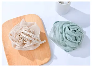 Detail view of two rose-shaped mesh bath sponges in cream and green on a wooden tray.