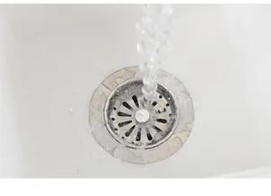 Nahaufnahme des Spülensiebs aus Edelstahl mit fließendem Wasser zum Haarefangen
