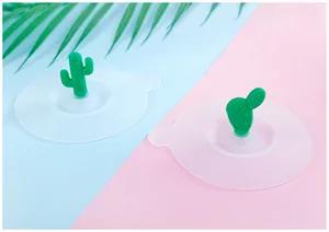 Detailed view of two cute green cactus silicone cup lids on a blue and pink decorative background