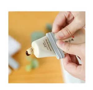 Detailopname van een grijze handmatige tubeknijper die een crème-tube leegmaakt.