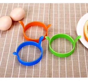 Trois anneaux à œufs ronds en silicone coloré sur une nappe à carreaux avec œufs