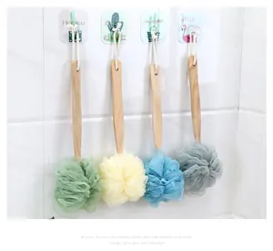 Four colorful bath sponges with wooden long handles hanging on tiled bathroom wall