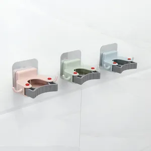 Set di tre supporti a muro autoadesivi per scope e mocio in vari colori pastello.