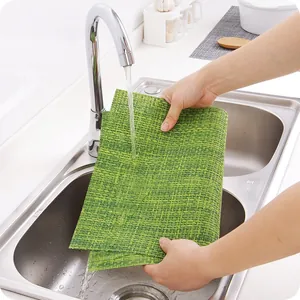 Green woven heat-resistant table mat being washed under running water in a kitchen sink