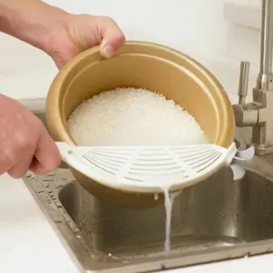 White clip-on pot strainer and rice washer tool shown draining water from a gold rice pot