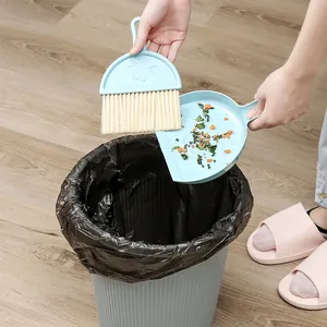 Light blue mini desktop broom and dustpan set being used to sweep debris into a bin