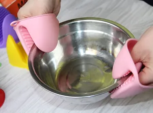 Handen die roze hittebestendige siliconen ovenwanten gebruiken om een kom op te tillen