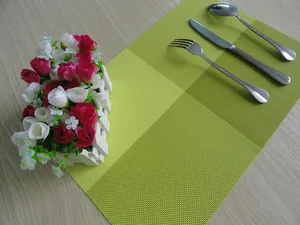 Top view of green grid PVC placemat with cutlery and flowers on wooden table