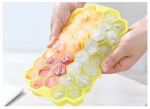 Handheld yellow silicone honeycomb ice tray filled with various frozen fruit cubes