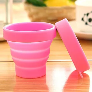 Detail view of pink portable collapsible silicone travel cup with lid on wooden table
