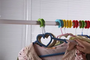 Détail de crochets coupe-vent colorés fixant solidement des cintres sur une barre de séchage