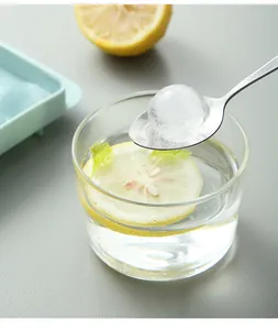 Macro shot of a clear spherical ice ball on a spoon over a lemon water glass.