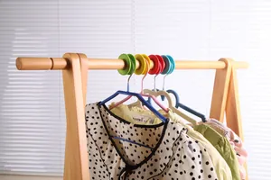 Détail de clips coupe-vent colorés fixant solidement des cintres sur une tringle en bois.