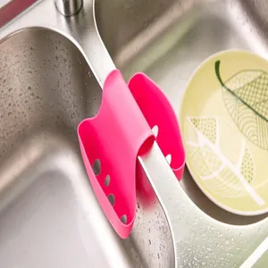 Pink saddle-style silicone sink sponge holder hanging in a kitchen double sink setup