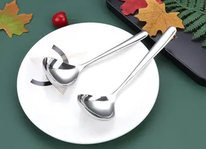 Close-up of two polished stainless steel long handle soup ladles on a white plate.