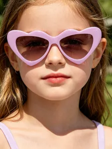 A young girl models vibrant purple heart-shaped sunglasses in sunny outdoor lighting.