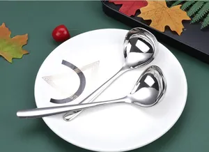 Detailed macro view of polished stainless steel soup ladles with long handles on a ceramic plate