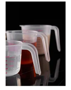 Macro view of three transparent measuring cups with red scales on a sleek black background.
