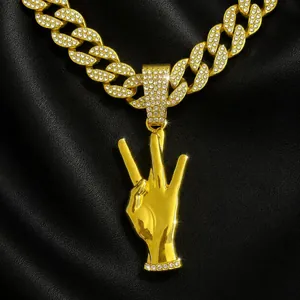 Detalle de collar hip hop dorado con colgante de gesto de tres dedos sobre cuero negro.