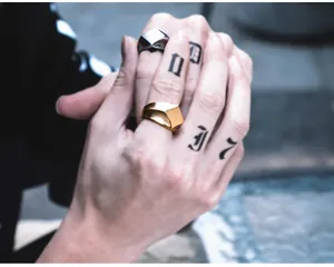 Makroaufnahme von retro-geometrischen Ringen in Gold und Silber auf tätowierten Fingern.