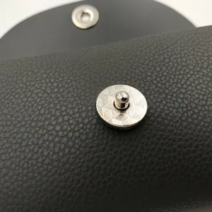 Close-up view of a durable metal snap button on a vintage black leather glasses case