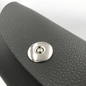 Close-up view of a grey lychee grain leather glasses case with a silver metal snap button.