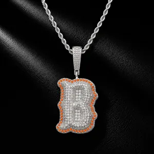 Detailed close-up of iced out bone-shaped letter B pendant with orange zircon border