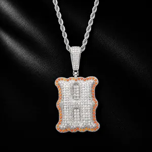 Detailed view of an iced out letter H pendant necklace with orange accents