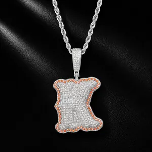 Close-up detail of iced out letter K pendant with orange stone border on rope chain