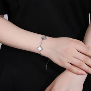 Close-up detail of a minimalist silver-toned bracelet with square mother-of-pearl charms on wrist
