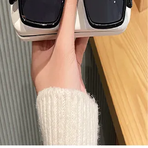 Vista detallada de gafas de sol cuadradas de gran tamaño blanco crema en la mano