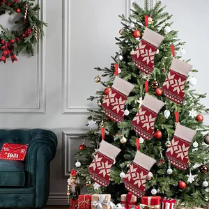 Set of six red and white knitted Christmas stockings with snowflake patterns on a tree.