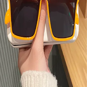 Vista detallada de gafas de sol cuadradas naranjas de moda sostenidas por la mano.