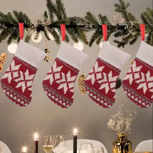 Four knitted Christmas stockings hanging on a pine garland with warm festive lighting.