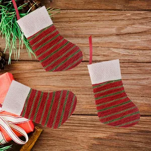 Three mini red and green striped knitted Christmas stockings on a festive wooden background.