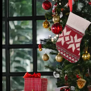 Red and white knitted Christmas stocking hanging on a tree with snowflake pattern