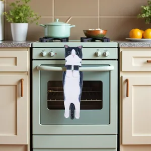 Realistic black and white cat hand towel hanging on a green oven handle in a kitchen.